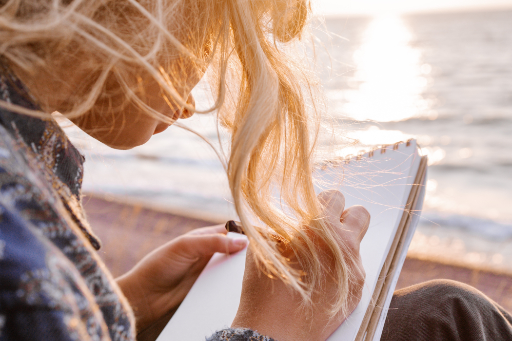 Eine Frau mit blonden Haaren schreibt in ein Notizbuch, Strand, Sonne